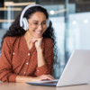 Young beautiful woman in headphones working with laptop inside office at workplace.
