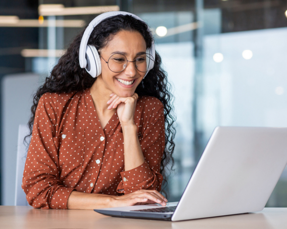 Young beautiful woman in headphones working with laptop inside office at workplace.
