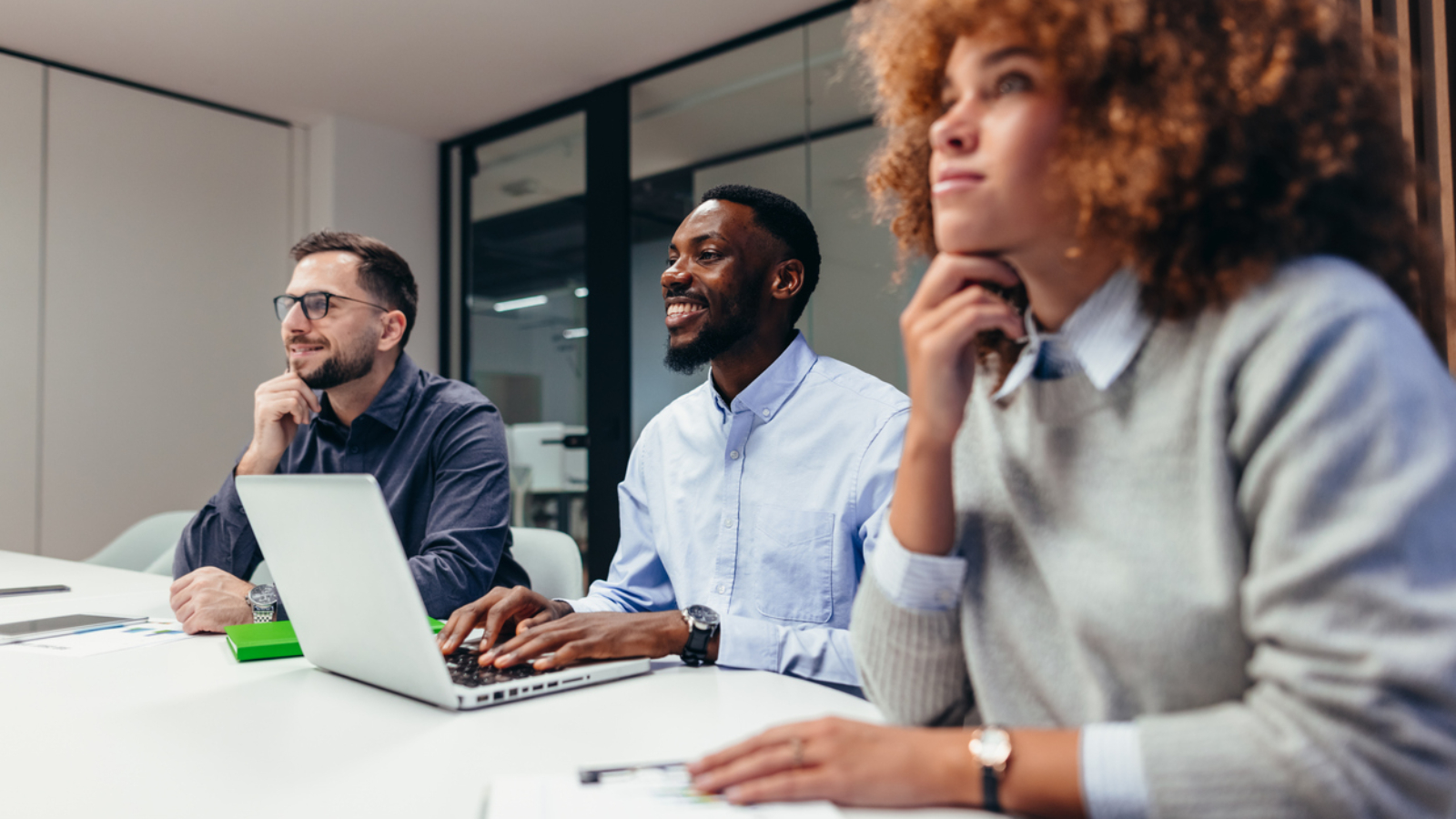 Group of businesspeople engaged in a corporate meeting, listening attentively to a presentation while a man takes notes on his laptop, fostering collaboration and teamwork
