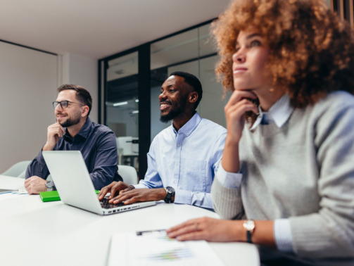Group of businesspeople engaged in a corporate meeting, listening attentively to a presentation while a man takes notes on his laptop, fostering collaboration and teamwork