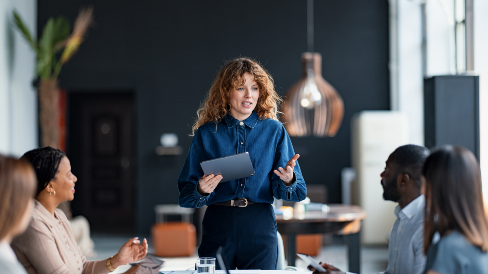 Confident businesswoman presents to a diverse team during a collaborative meeting in a stylish office environment, promoting teamwork and communication.