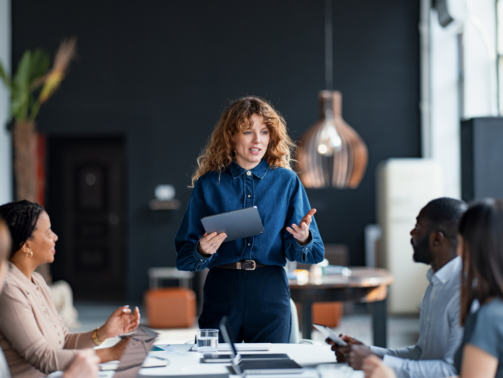Confident businesswoman presents to a diverse team during a collaborative meeting in a stylish office environment, promoting teamwork and communication.