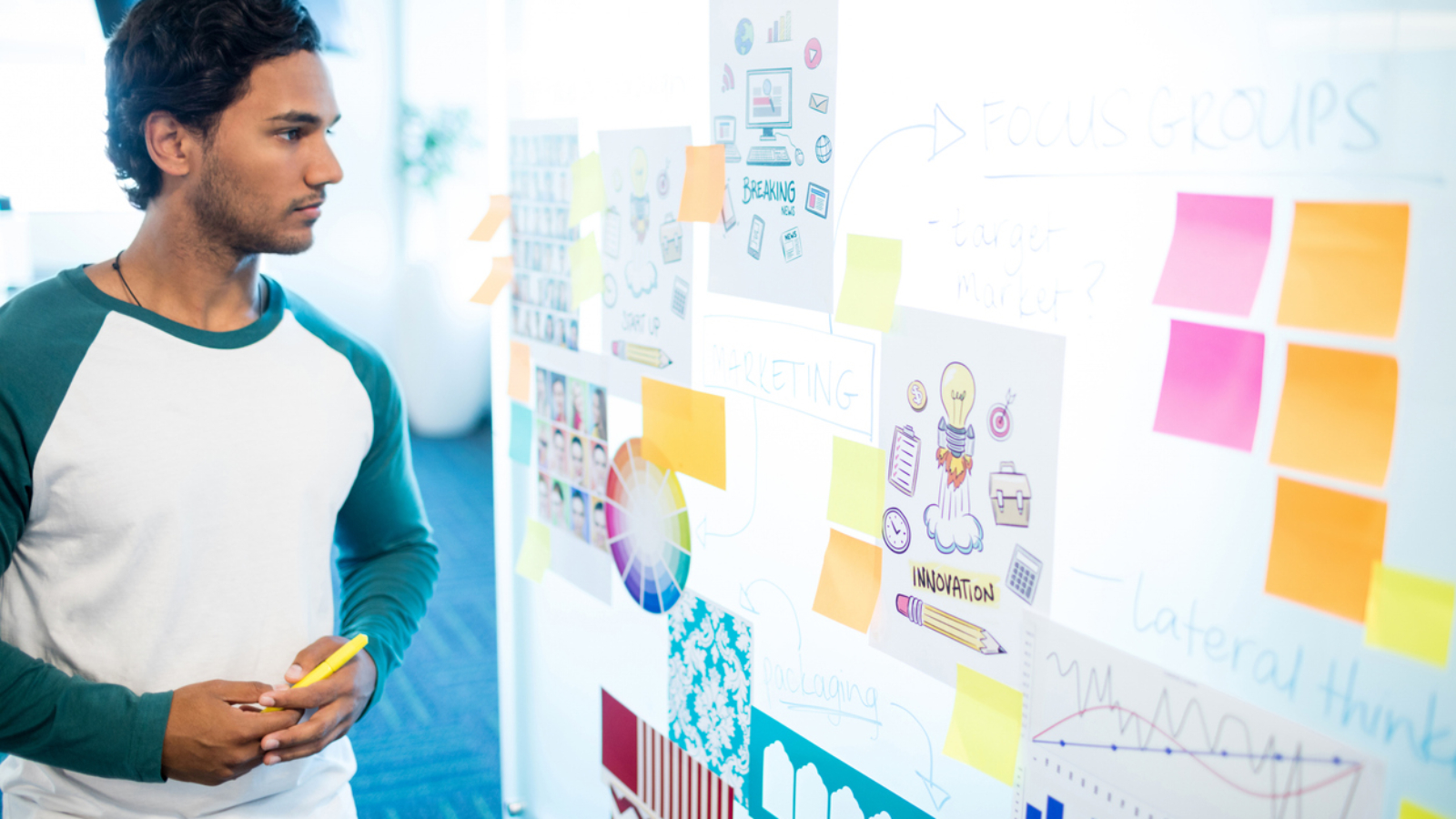 Thoughtful man looking at sticky notes and charts in office