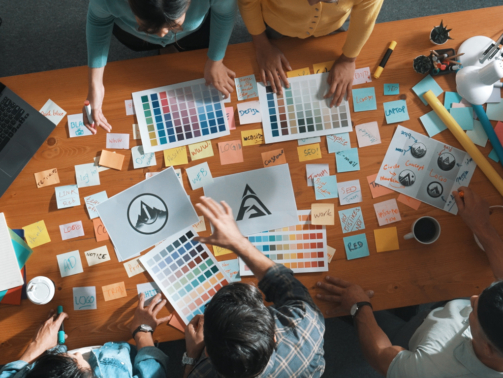 Top view of business team write graphic logo on meeting table with colorful sticky notes and design while explain idea. Project manager sharing idea and explain concept art to smart team. Symposium.