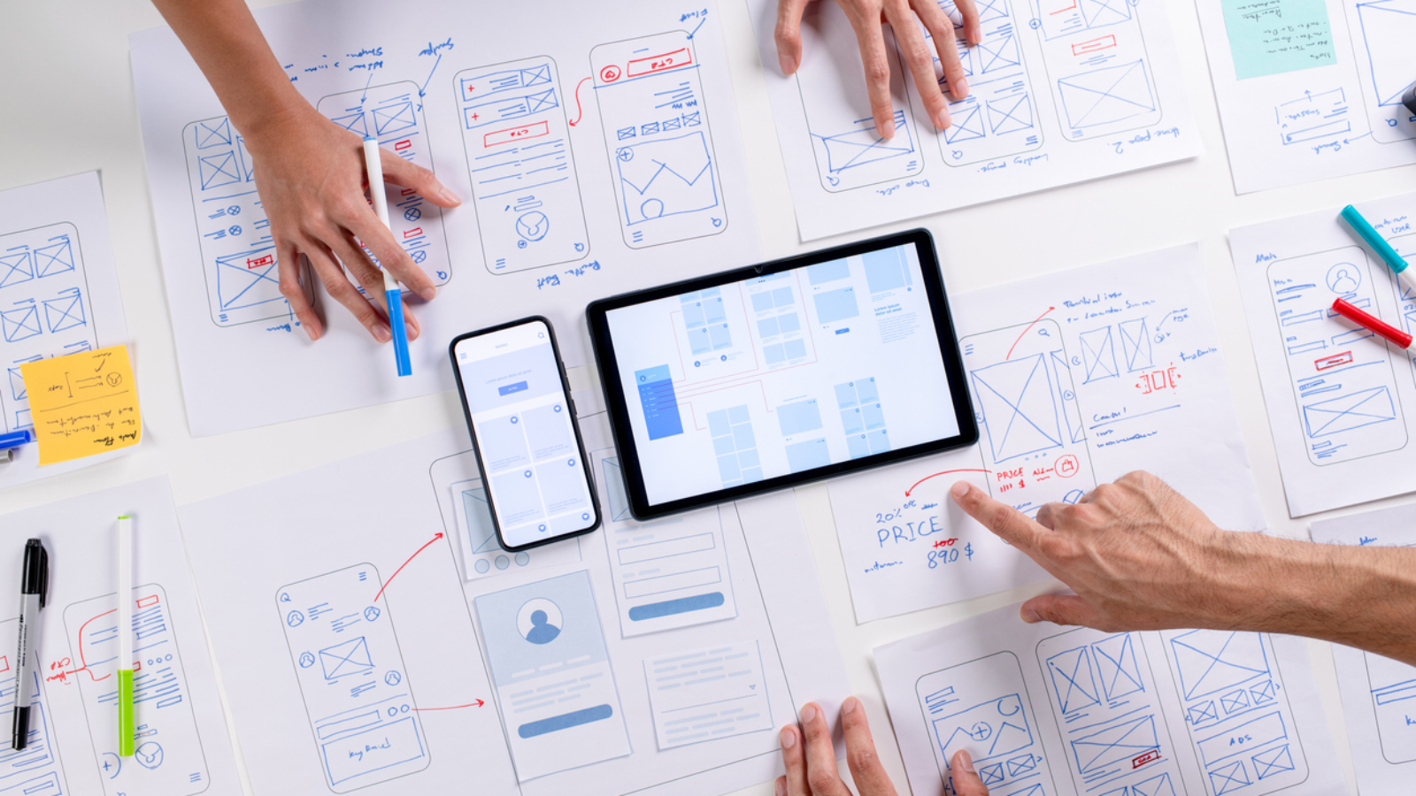 UX/UI designers discussing and brainstorming on wireframes for a website and mobile app prototype, surrounded by sketches of user flow and design tools, in the concept of website and mobile application design concept.