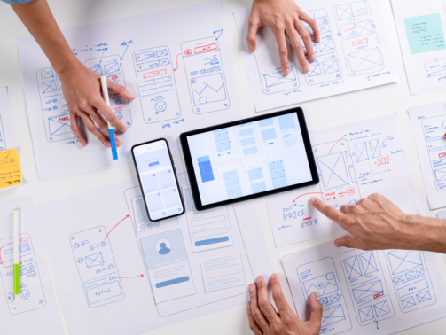 UX/UI designers discussing and brainstorming on wireframes for a website and mobile app prototype, surrounded by sketches of user flow and design tools, in the concept of website and mobile application design concept.