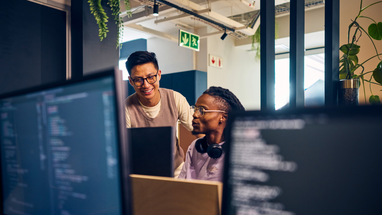 Two diverse software developers collaborating on a project, reviewing code on computer screens in a contemporary office space