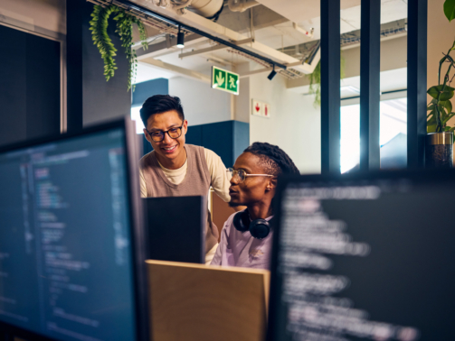 Two diverse software developers collaborating on a project, reviewing code on computer screens in a contemporary office space