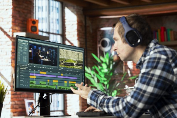 Freelancing video editor in home office wearing headphones to polish raw footage and improve audio quality. Videographer professionally adjusting clips, applying sound effects to film
