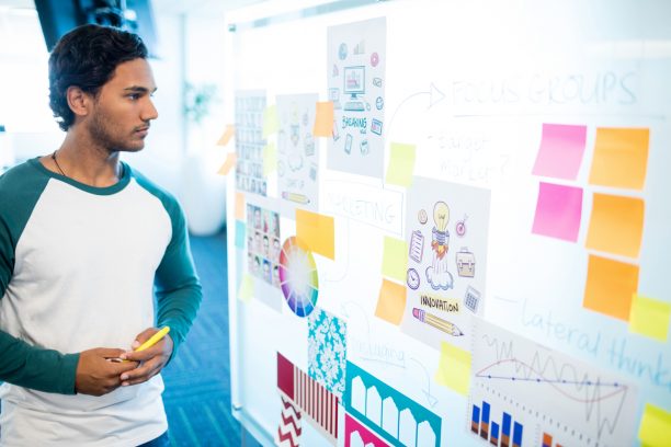 Thoughtful man looking at sticky notes and charts in office
